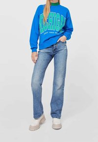Sudadera azul con el texto verde "MICHIGAN" y "GREAT LAKES STATE," combinada con jeans de mezclilla azul claro y zapatos de plataforma beige.