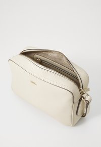 Borsa zip in pelle crema con superficie texturizzata, rifiniture marroni e accessori dorati. Presenta una tasca interna per l'organizzazione.