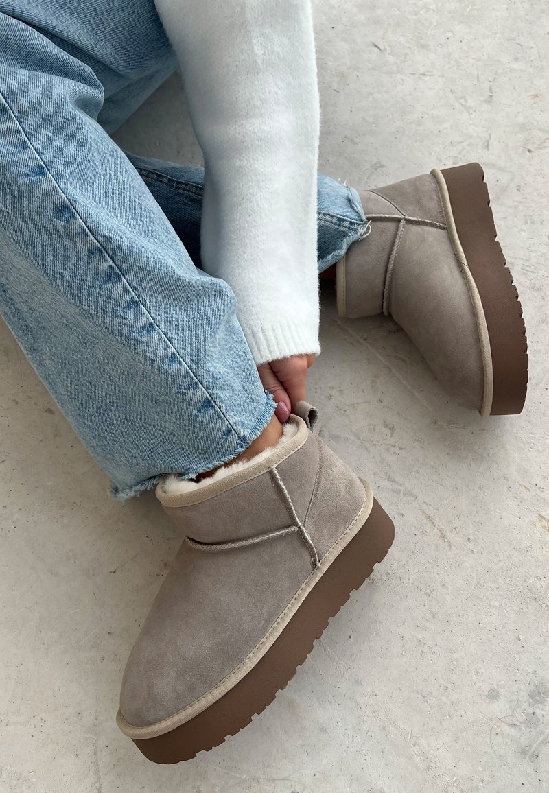 Bottines en daim grises avec une doublure en peluche, des accents beiges, un bout rond et une semelle brune robuste, accompagnées de jeans en denim bleu clair.