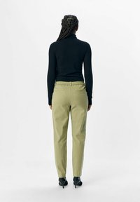 Must must sleeves, hele rohelised püksid elastse vöökojaga, kaks tagakotti, kombineeritud mustade kõrgete kontsadega kingadega.