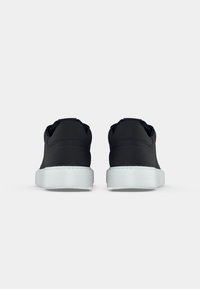 Zwarte sneakers met een gladde, matte afwerking, voorzien van een witte rubberen zool. Rond formaat met minimale details en stiksels.