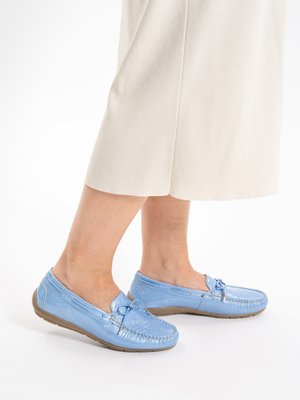 Feet wearing light blue leather moccasins with bow details, paired with cream-colored pants.