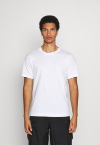 Camiseta de algodón blanca de manga corta con cuello redondo. Textura suave, corte regular, combinada con pantalones cortos cargo negros de diseño liso.