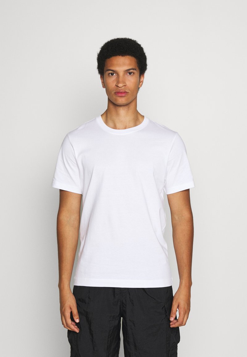 Camiseta de algodón blanca de manga corta con cuello redondo. Textura suave, corte regular, combinada con pantalones cortos cargo negros de diseño liso.