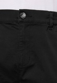 Pantaloni in cotone nero con una texture liscia, dotati di chiusura con bottone in vita e cuciture visibili lungo la tasca laterale.