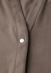 Hnědá semišová tkanina s hladkým povrchem, se stříbrným patentkem uprostřed a viditelným prošíváním podél okrajů.