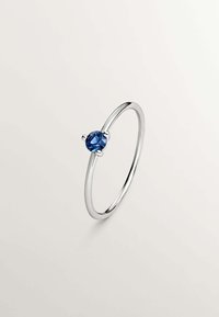Anillo de plata con una piedra preciosa azul redonda en el centro, montada en una configuración de cuatro garras, con un diseño de banda suave y minimalista.