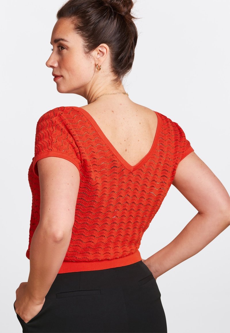 Top de punto rojo con espalda en V, mangas cortas y un patrón de ondas texturizado. Presenta un dobladillo ajustado y una banda sólida en color contrastante.
