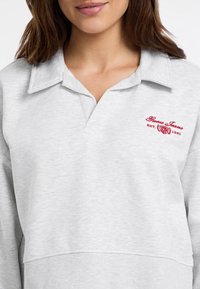 Hellgrauer Sweatshirt mit Kragen, geripptem Saum und gesticktem roten Logodesign. Weiche Textur, lässige Passform und lange Ärmel.