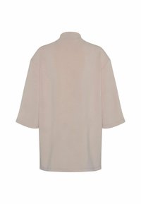 Beige oversized tričkoa s krátkým rukávem a vysokým límečkem, zobrazené zezadu na bílém pozadí.