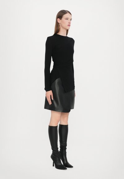 Schwarzes Longsleeve-Oberteil mit gedrehtem Design, kombiniert mit einem Lederminirock. Knielange schwarze High Heels runden den Look ab. Insgesamt glatte Textur.