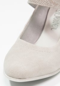 Beżowe buty zakryte palcami o zamszowej teksturze, okrągłym nosku i niskim obcasie; posiadają szeroki pasek wzdłuż górnej części.