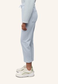 Světle modré, zkrácené tepláky s nastavovací šňůrkou v pase, bočními kapsami a měkkou texturou, v kombinaci s bílými a zelenými teniskami.