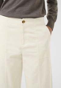Crèmegekleurde ribfluwelen broek met verticale ribbels, voorzien van een knoopsluiting, zijzakken en een licht ruime pasvorm.
