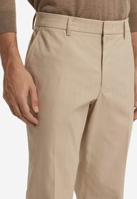 Tan chinos i texturerad tyg, med dragkedja, sidofickor och skräddarsydd passform med bälteshällor.