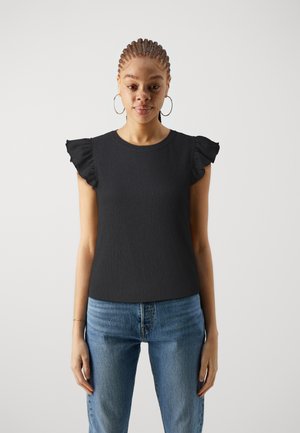 Haut court noir à manches courtes avec des épaules volantées, en tissu texturé, décolleté rond, associé à un jean bleu clair.