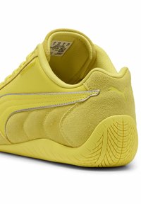Zapatilla Puma de ante y cuero amarilla mostrando el lateral, el talón, el patrón de la suela y la etiqueta de tamaño dentro del collar.