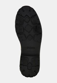 Czarna gumowa podeszwa buta z wzorzystym bieżnikiem, z logo "GUESS" oraz wytłoczonym oznaczeniem rozmiaru "37" na powierzchni.