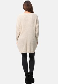 Beiger, gestrickter Pullover mit langen Ärmeln, lässigem Schnitt, strukturiertem Design und abgerundetem Saum, kombiniert mit schwarzen Skinny-Jeans und Stiefeletten mit Absatz.