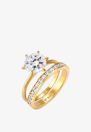 Set van gouden ring met een grote ronde heldere steen in een zesgrijper en een tweede band versierd met kleinere heldere stenen.