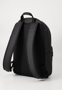 Black backpack with a smooth exterior, padded mesh back, and adjustable straps. Features a top handle and side zip pocket.