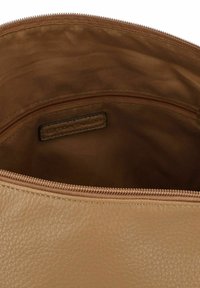Intérieur d'un sac en cuir tan avec une texture lisse, fermeture éclair et une petite étiquette visible à l'intérieur. Couleur douce et neutre.