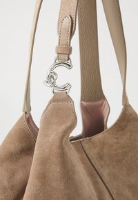 Borsa in suede beige con una tracolla in pelle texturizzata. Presenta un accento in metallo argentato e una fodera interna liscia rosa.