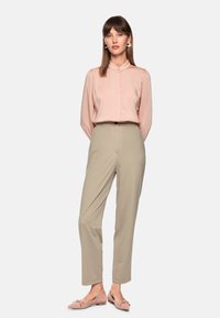 Light pink long-sleeve blouse with a collar, paired with beige tapered pants and pink flats featuring bow accents. Smooth fabric textures throughout.
