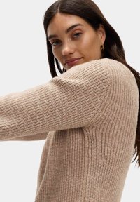 Béžový pletený svetr s texturovaným jemným designem, se širokým střihem a mírně spuštěnými rameny, z měkkého a útulného materiálu.