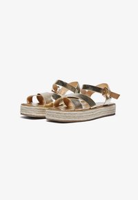 Metalliske gull espadriller med kryssremmer, vevd juteplattform og justerbar ankelspenne. Glatt tekstur, åpne tær.