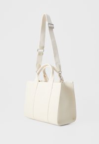 Sac à main en toile blanche avec deux poignées supérieures et une bandoulière amovible. Présente des lignes épurées et une forme structurée. Design minimaliste.