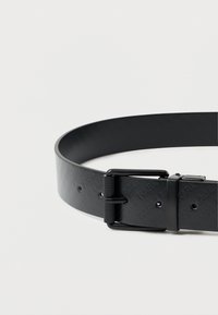 Μαύρη δερμάτινη ζώνη με λεία επιφάνεια, που διαθ�έτει υφασμάτινη υφή, ορθογώνια μεταλλική αγκράφα και αρκετές τρύπες ρύθμισης.