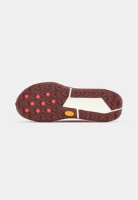 Semelle de chaussure avec une bande de roulement en caoutchouc marron présentant des crampons en forme de flèche et des inserts circulaires rouges, et une section de semelle intermédiaire blanche.