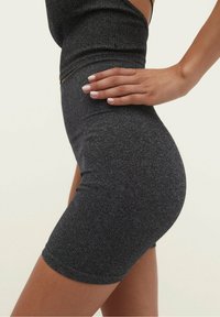 Primer plano de una persona que lleva pantalones cortos de tiro alto texturizados en gris oscuro con una parte superior a juego, con la mano apoyada en la cadera.