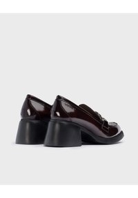 Zapatos de cuero burdeos brillantes con punta cuadrada y detalle de hebilla decorativa. Presentan un tacón grueso negro para estabilidad y estilo.