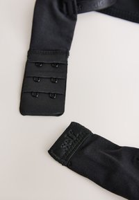 Must rinnahoidja tagumine kinnis, kus on kolm rida kahest konksust ja kangast rihmad heledal taustal.