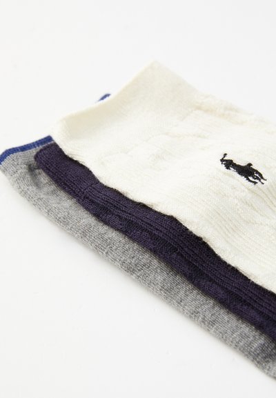 Trois paires de chaussettes : crème, gris foncé et marine. Tricot texturé avec un petit logo noir sur la paire crème. Finition lisse, largeurs variées.