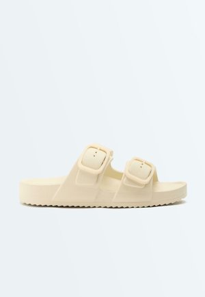 Beige open-toe slide sandal with two adjustable buckle straps and a textured sole for grip.