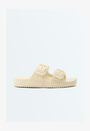 Bézs nyitott orrú papucs két állítható csattal és texturált talppal a jobb tapadásért.