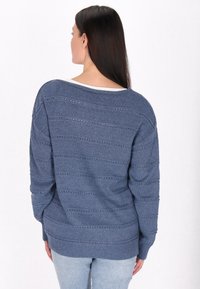 Túlméretezett kék kötött pulóver, texturált mintával, nyitott csíkokkal és hosszú ujjakra. Bordázott alj a kiegészítő részletekért.