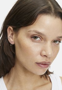 Silberne Creolen mit glatter Oberfläche, die ein kleines Cuff-Detail aufweisen. Am linken Ohr des Modells getragen und zeigen ein minimalistisches Design.