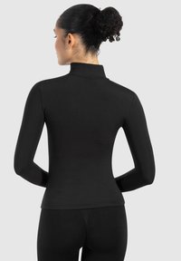 Fitted black long-sleeve top with a high collar. Smooth texture, minimal design, and seamless construction. Styled with matching black leggings.