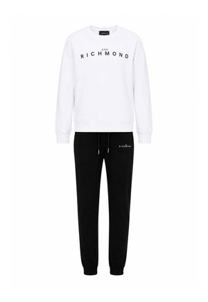 Felpa bianca a maniche lunghe con testo "John Richmond" sopra pantaloni da tuta neri con coulisse e piccolo logo "John Richmond" sulla coscia sinistra.