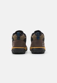 Chaussures de randonnée marron et noires avec une tige en maille texturée, une semelle en caoutchouc, et des accents jaunes sur la semelle pour une meilleure adhérence.