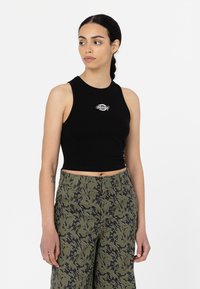 Top court noir en tissu lisse, avec un petit logo blanc sur la poitrine, associé à un pantalon vert camouflé.