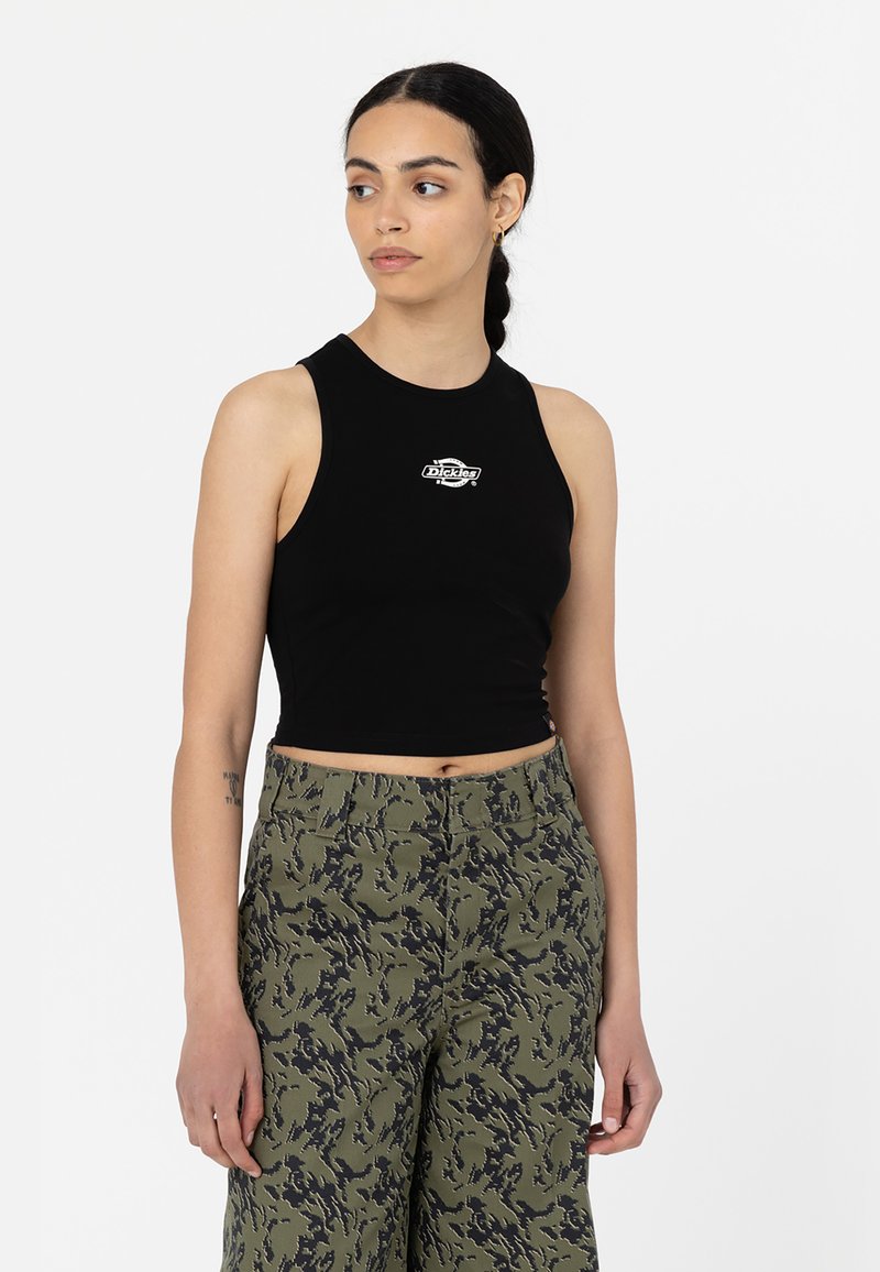 Top court noir en tissu lisse, avec un petit logo blanc sur la poitrine, associé à un pantalon vert camouflé.