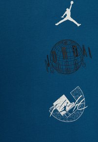 Modré bavlněné tričko s bílou grafikou: skákající postava, vzor globusu s textem "JORDAN" a kruhový design s "FLIGHT."