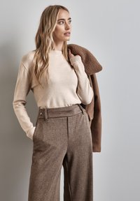 Beige stickad tröja med ribbade manschetter i kombination med bruna mönstrade vida byxor, som har en skräddarsydd passform och sidofickor.