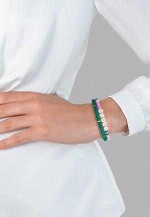 Braccialetti colorati di perline in verde, viola e bianco con lettere, indossati su un polso. Le perline sono lisce con una finitura lucida.