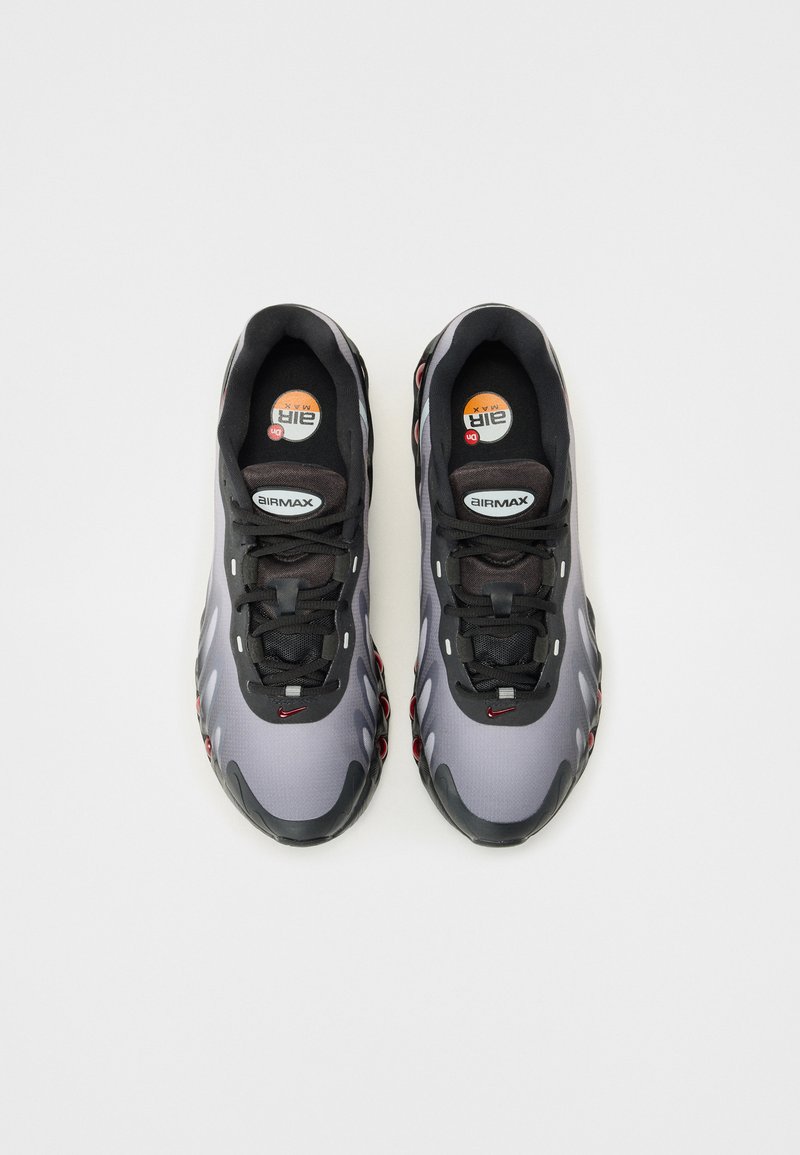 Graue und schwarze Sportschuhe mit strukturiertem Finish, ausgestattet mit einem gepolsterten Kragen, schwarzen Schnürsenkeln und roten Akzenten an der Sohle und den Seiten.